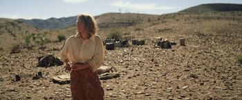 Movie still from “Tracks” (2013), directed by John Curran – A woman standing on a dry grass covered field; Wide shot, Over the shoulder angle