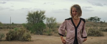 Movie still from “Tracks” (2013), directed by John Curran – A woman in a pink and black shirt standing in a field; Medium shot, Low angle