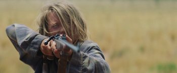 Movie still from “Tracks” (2013), directed by John Curran – A person holding a gun in a field; Close Up shot, Over the shoulder angle