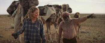 Movie still from “Tracks” (2013), directed by John Curran – A man and a woman standing in front of a herd of camels; Medium shot, Over the shoulder angle
