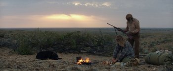 Movie still from “Tracks” (2013), directed by John Curran – A woman sitting on the ground next to a fire; Wide shot, Over the shoulder angle