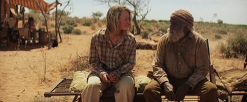 Movie still from “Tracks” (2013), directed by John Curran – A woman sitting next to an older man in a field; Medium shot, Over the shoulder angle