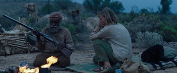 Movie still from “Tracks” (2013), directed by John Curran – A man and a woman sitting on the ground near a fire; Medium shot, Over the shoulder angle