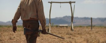 Movie still from “Tracks” (2013), directed by John Curran – A man holding a pair of pliers standing in the middle of an open field; Medium shot, Over the shoulder angle