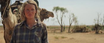 Movie still from “Tracks” (2013), directed by John Curran – A woman standing next to a camel in the desert; Medium shot, Low angle