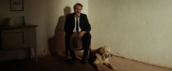 Movie still from “Tracks” (2013), directed by John Curran – A man sitting on a chair next to a dog; Wide shot, Low angle