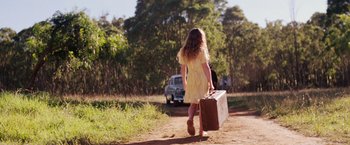 Movie still from “Tracks” (2013), directed by John Curran – A woman in a yellow dress carrying a brown suitcase; Wide shot, Over the shoulder angle