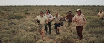 Movie still from “Tracks” (2013), directed by John Curran – A group of men running through a field of grass; Wide shot, High angle