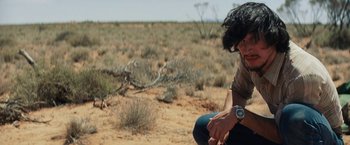 Movie still from “Tracks” (2013), directed by John Curran – A man sitting in the middle of an open field; Medium shot, Over the shoulder angle