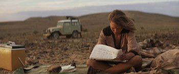Movie still from “Tracks” (2013), directed by John Curran – A woman sitting on the ground reading a newspaper; Medium shot, Over the shoulder angle
