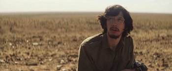 Movie still from “Tracks” (2013), directed by John Curran – A man with glasses sitting in the middle of an open field; Close Up shot, Over the shoulder angle