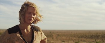 Movie still from “Tracks” (2013), directed by John Curran – A young woman standing in a field near a forest; Close Up shot, Low angle