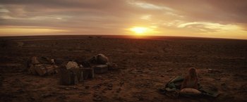 Movie still from “Tracks” (2013), directed by John Curran – The sun is setting in the desert with people sitting in the background; Extreme Wide shot, High angle
