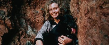 Movie still from “Tracks” (2013), directed by John Curran – A woman holding a black dog in her arms in front of a rock wall; Close Up shot, High angle