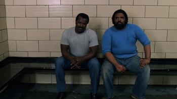 Movie still from “Trading Places” (1983), directed by John Landis – A couple of men sitting next to each other on top of a bench; Wide shot, Low angle