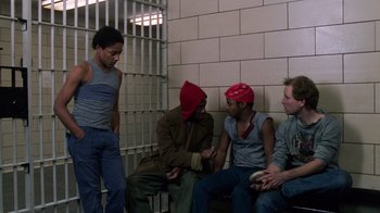 Movie still from “Trading Places” (1983), directed by John Landis – A group of men sitting next to each other in front of a wall; Medium shot, Low angle