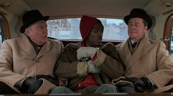 Movie still from “Trading Places” (1983), directed by John Landis – Three men sitting in the back seat of a car; Medium shot, High angle