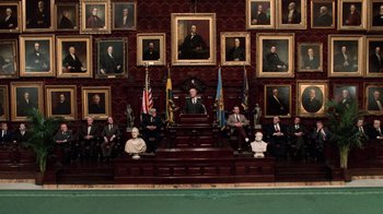 Movie still from “Trading Places” (1983), directed by John Landis – A group of people sitting in front of a man on a chair; Extreme Wide shot, High angle
