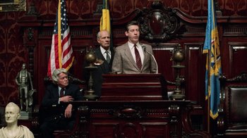 Movie still from “Trading Places” (1983), directed by John Landis – A man is speaking at a podium in a courtroom; Medium shot, Low angle