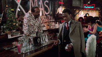 Movie still from “Trading Places” (1983), directed by John Landis – Two men are standing at a bar and one of the men is holding a cigarette; Medium shot, Over the shoulder angle