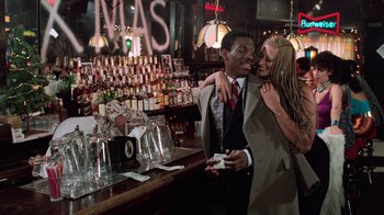 Movie still from “Trading Places” (1983), directed by John Landis – A man and a woman are hugging in front of a bar; Wide shot, Over the shoulder angle