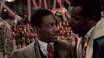 Movie still from “Trading Places” (1983), directed by John Landis – A man in a suit and tie next to another man in a suit and tie; Close Up shot, Over the shoulder angle
