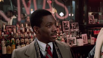 Movie still from “Trading Places” (1983), directed by John Landis – A man wearing a suit and tie in a bar; Close Up shot, Over the shoulder angle