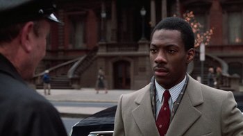 Movie still from “Trading Places” (1983), directed by John Landis – A man wearing a suit and tie standing in front of a building; Close Up shot, Over the shoulder angle