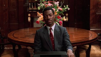 Movie still from “Trading Places” (1983), directed by John Landis – A man in a suit and tie sitting at a table; Medium shot, High angle