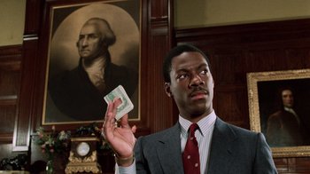 Movie still from “Trading Places” (1983), directed by John Landis – A man in a suit and tie holding up a dollar bill in front of a portrait of george washington; Medium shot, Low angle