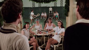 Movie still from “Trading Places” (1983), directed by John Landis – A group of women sitting at a table with tennis rackets; Wide shot, Over the shoulder angle