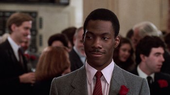 Movie still from “Trading Places” (1983), directed by John Landis – A man wearing a suit and tie in front of a group of people; Close Up shot, Low angle