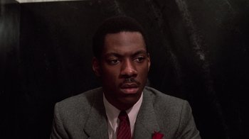 Movie still from “Trading Places” (1983), directed by John Landis – A man wearing a suit and tie sitting in front of a wall; Close Up shot, High angle