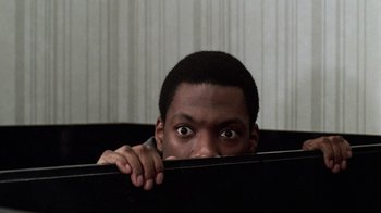 Movie still from “Trading Places” (1983), directed by John Landis – A man hiding his face behind a black object; Close Up shot, Low angle
