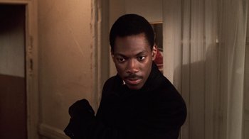Movie still from “Trading Places” (1983), directed by John Landis – A man in a black shirt is standing in a room; Close Up shot, High angle