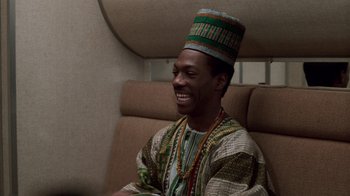 Movie still from “Trading Places” (1983), directed by John Landis – A man wearing a colorful hat sitting on a couch; Medium shot, High angle