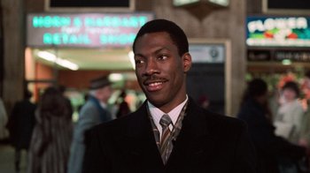 Movie still from “Trading Places” (1983), directed by John Landis – A man wearing a suit and tie smiling for the camera; Close Up shot, Low angle