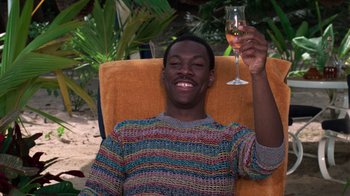 Movie still from “Trading Places” (1983), directed by John Landis – A man sitting in a chair holding up a glass of wine; Medium shot, High angle