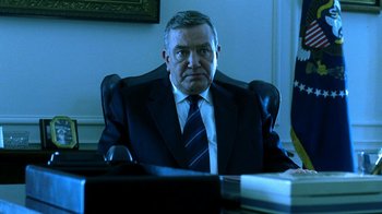 Movie still from “Traffic” (2000), directed by Steven Soderbergh – A man sitting at a desk wearing a suit and tie; Medium shot, Low angle