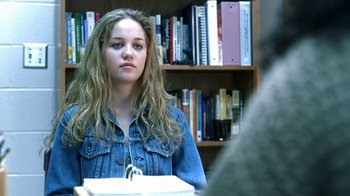Movie still from “Traffic” (2000), directed by Steven Soderbergh – A woman sitting at a table in front of a bookshelf; Close Up shot, Over the shoulder angle