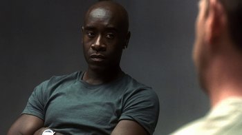 Movie still from “Traffic” (2000), directed by Steven Soderbergh – A man sitting in front of a wall with his arms crossed; Close Up shot, Low angle