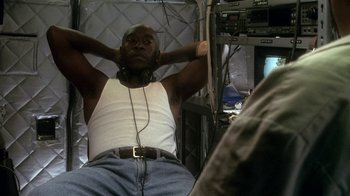 Movie still from “Traffic” (2000), directed by Steven Soderbergh – A man sitting on a chair with his hands behind his head; Medium shot, Low angle