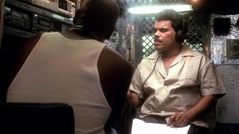 Movie still from “Traffic” (2000), directed by Steven Soderbergh – A man wearing headphones talking to another man in front of a microphone; Medium shot, Over the shoulder angle