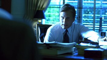 Movie still from “Traffic” (2000), directed by Steven Soderbergh – A man sitting at a table in front of a stack of papers; Medium shot, Over the shoulder angle