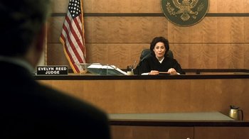 Movie still from “Traffic” (2000), directed by Steven Soderbergh – A judge sitting in front of a flag in a courtroom; Medium shot, Low angle