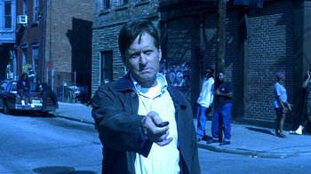 Movie still from “Traffic” (2000), directed by Steven Soderbergh – A man holding a cell phone while standing on the side of the street; Medium shot, Low angle