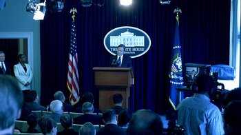 Movie still from “Traffic” (2000), directed by Steven Soderbergh – A man standing at a podium in front of american flags; Wide shot, Low angle
