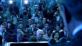 Movie still from “Traffic” (2000), directed by Steven Soderbergh – A group of people sitting in a room with microphones in front of them; Wide shot, Over the shoulder angle