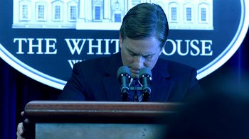 Movie still from “Traffic” (2000), directed by Steven Soderbergh – A man in a suit and tie sitting in front of microphones; Close Up shot, Over the shoulder angle