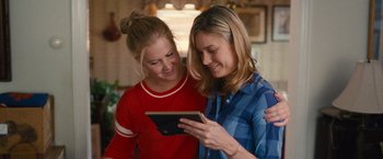Movie still from “Trainwreck” (2015), directed by Judd Apatow – Two young women looking at a tablet computer together; Close Up shot, Over the shoulder angle